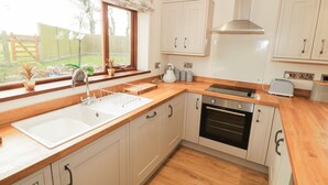 Una cocina con encimeras de madera, horno empotrado, pileta y muebles blancos.