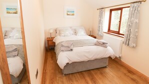 Un dormitorio con cama, mesitas de noche, una ventana con cortinas, un radiador y dos cuadros en la pared.