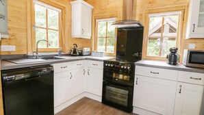 A modern kitchen with white cabinets, a black dishwasher, a stove, and a microwave. - Acorn Lodge (Saxmundham)