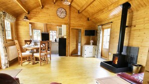A cozy wooden cabin interior with a dining area, kitchen, and a fireplace. - Acorn Lodge (Saxmundham)