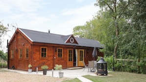 A wooden cabin with a front porch, a clock, and a garden area with a lawn and potted plants. - Acorn Lodge (Saxmundham)