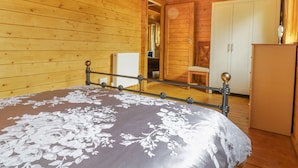 A wooden cabin bedroom with a bed, a wardrobe, and a small table. - Acorn Lodge (Saxmundham)