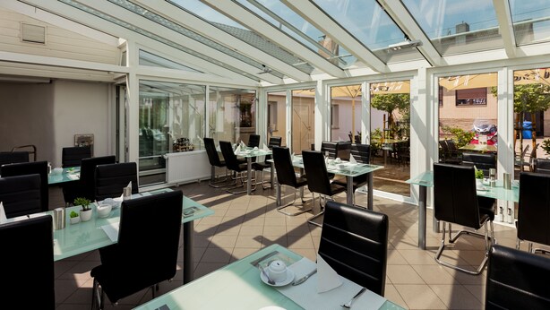 A restaurant with glass tables and chairs, a tiled floor, and a glass ceiling. - Hotel am Rosenplatz 24-hour check-in, free parking, guest kitchen (Rühen)