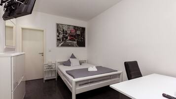 A modern bedroom with a bed, a desk, a chair, a TV, and a door.