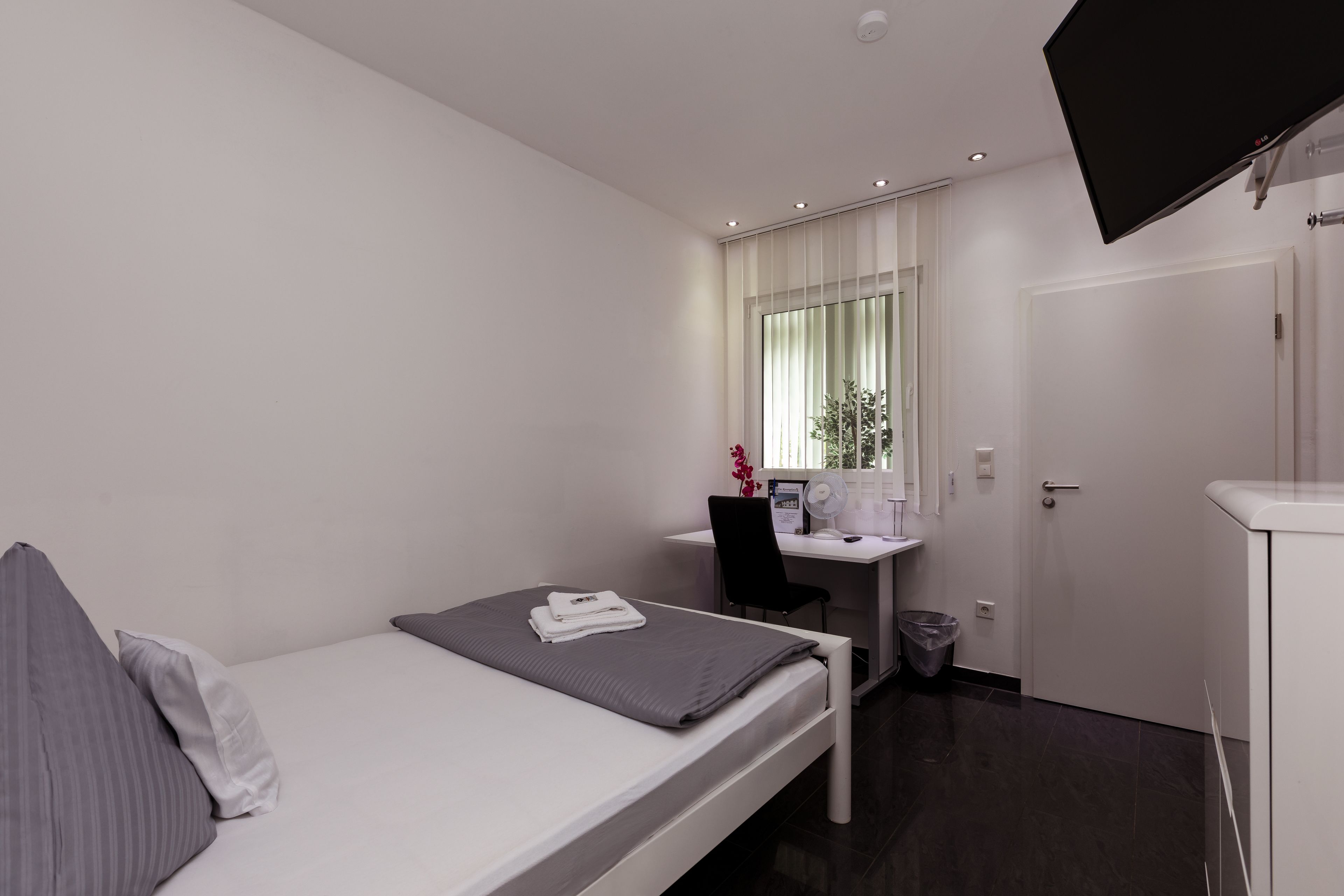 Una habitación de hotel moderna con una cama individual, un escritorio con ordenador, una silla y un televisor montado en la pared.