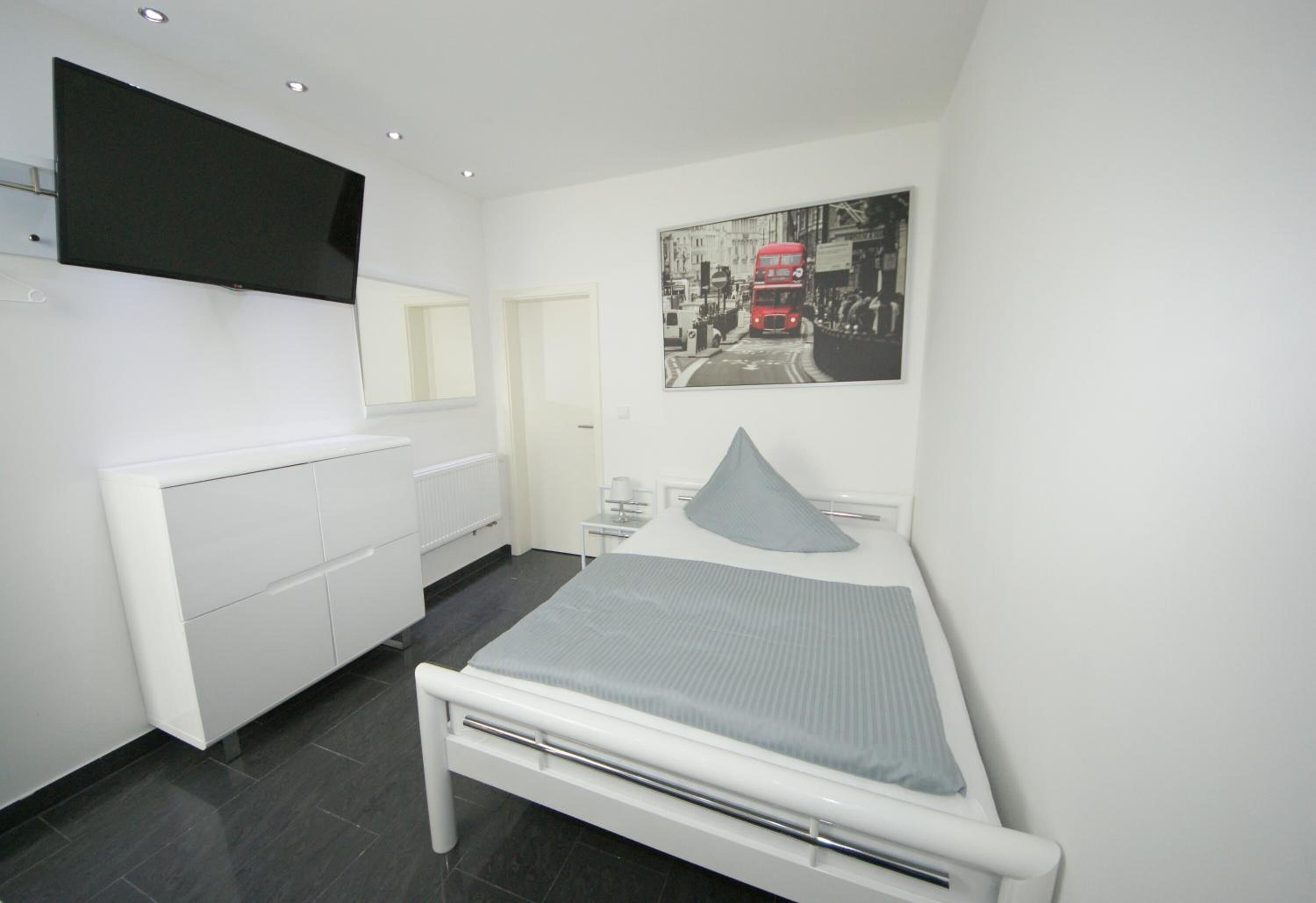 A modern bedroom with a bed, a bedside table, a TV mounted on the wall, and a poster of a red double-decker bus.
