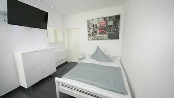 A modern bedroom with a bed, a bedside table, a TV mounted on the wall, and a poster of a red double-decker bus.
