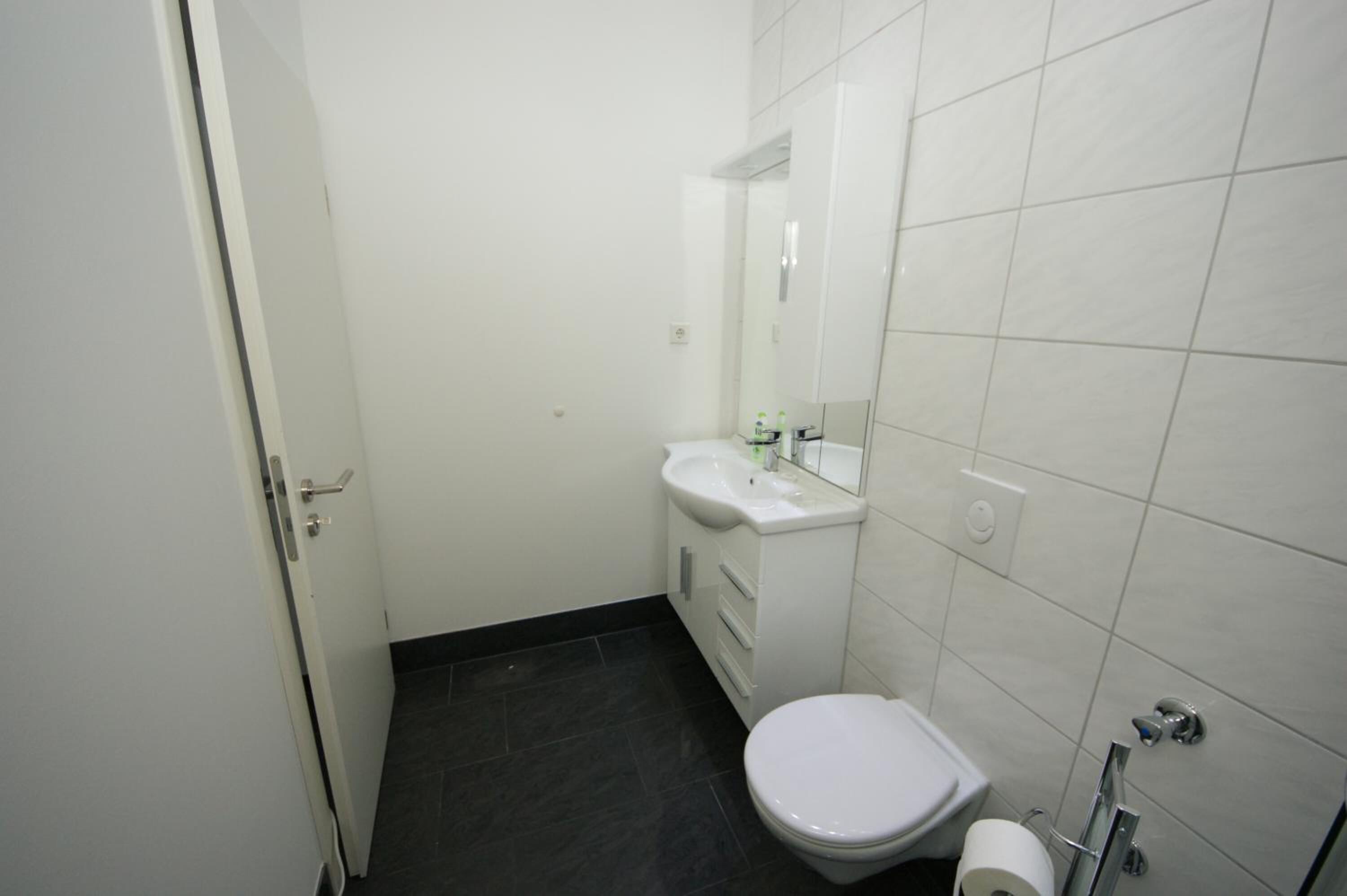 A small, clean bathroom with a white sink, mirror, and toilet.