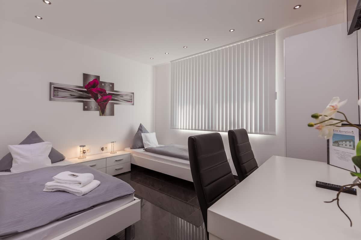 Une chambre d’hôtel moderne équipée d’un lit, de tables de chevet, d’un bureau et d’une fenêtre avec des stores.