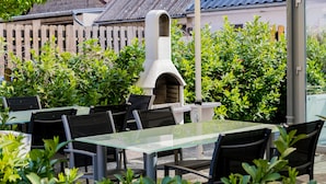 An outdoor dining area with tables and chairs, a stone oven, and lush greenery. - Hotel am Rosenplatz 24-hour check-in, free parking, guest kitchen (Rühen)