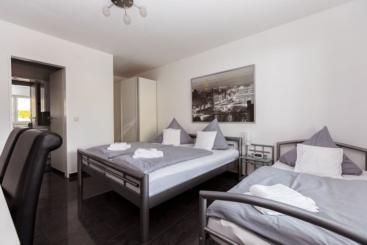 Une chambre d’hôtel moderne avec deux lits, une grande fenêtre et un tableau représentant un paysage urbain.