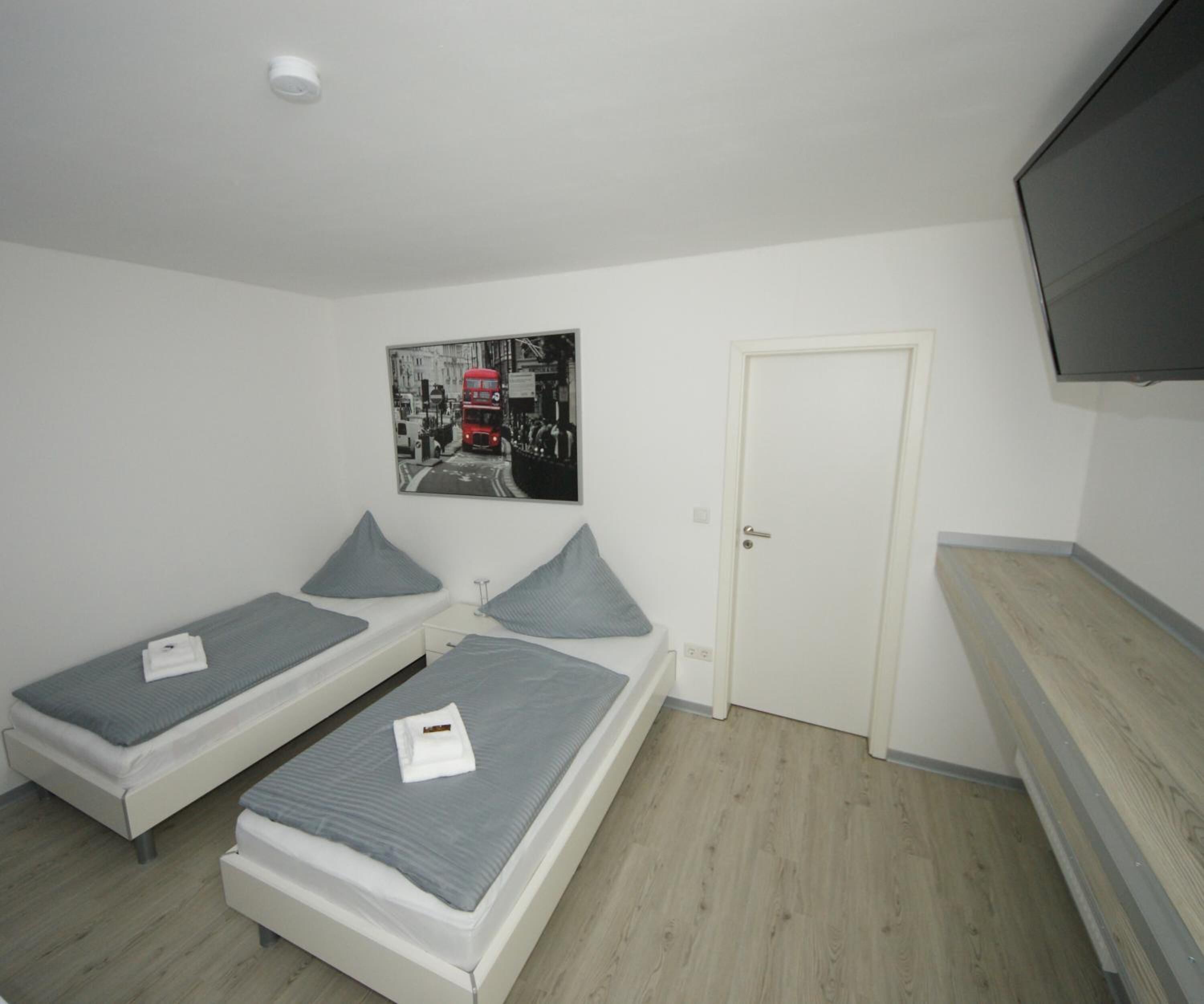Une chambre avec deux lits simples, une porte, un téléviseur à écran plat et une affiche au mur.