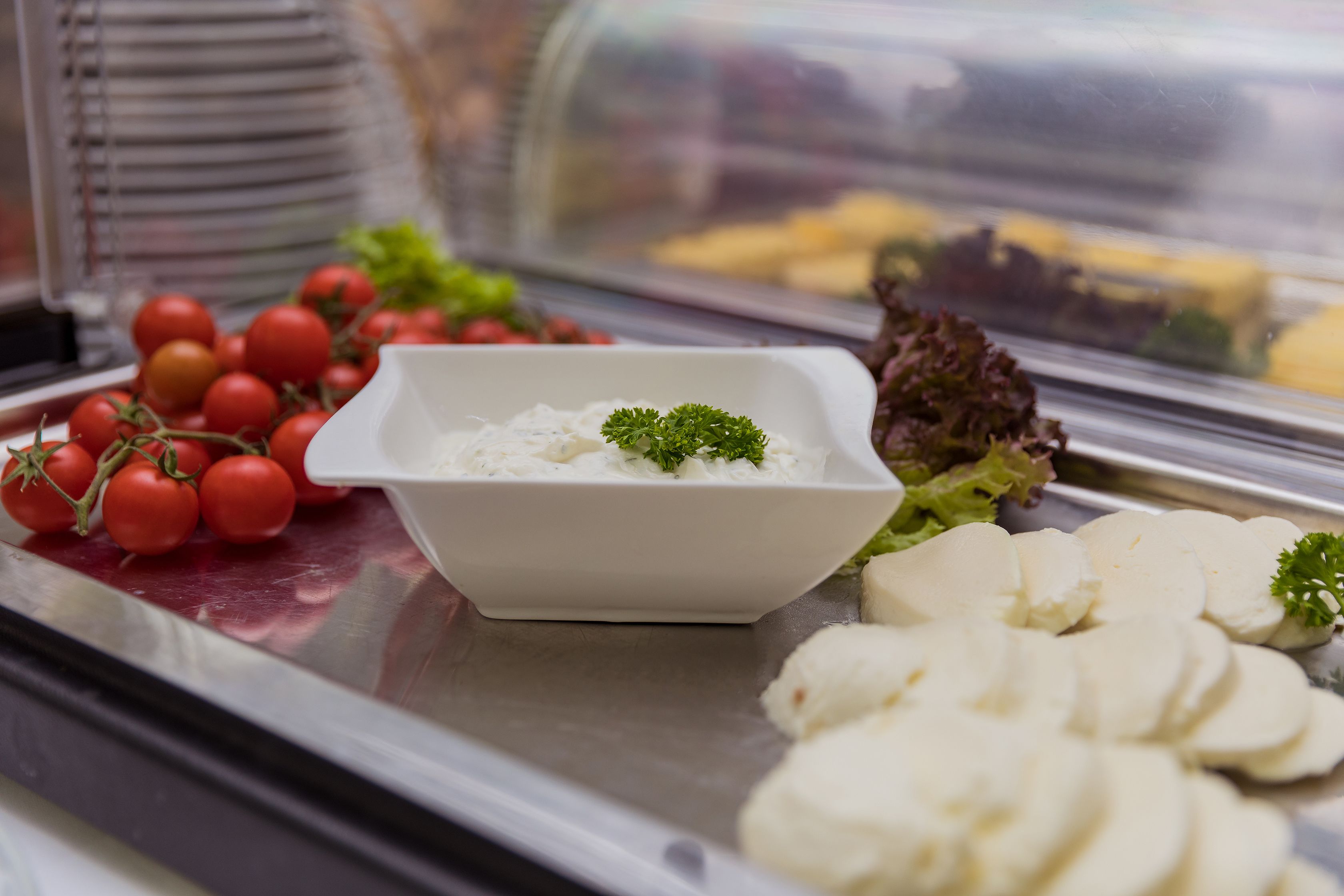 Un buffet proposant une variété d’aliments, notamment des tranches de fromage blanc, des tomates cerises et des légumes verts à feuilles.