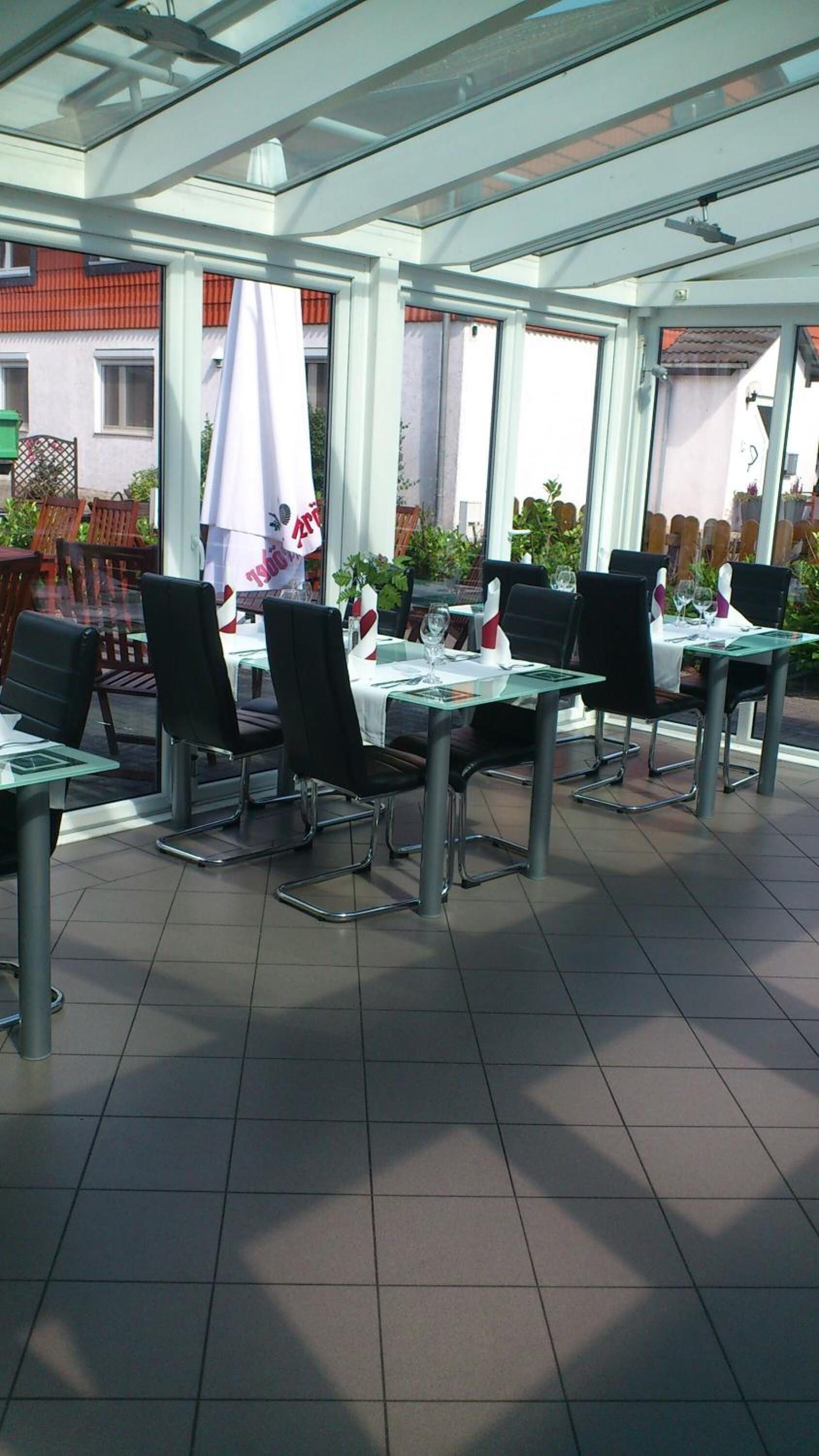 An outdoor patio area with tables and chairs, covered by a glass roof, and surrounded by a white fence.