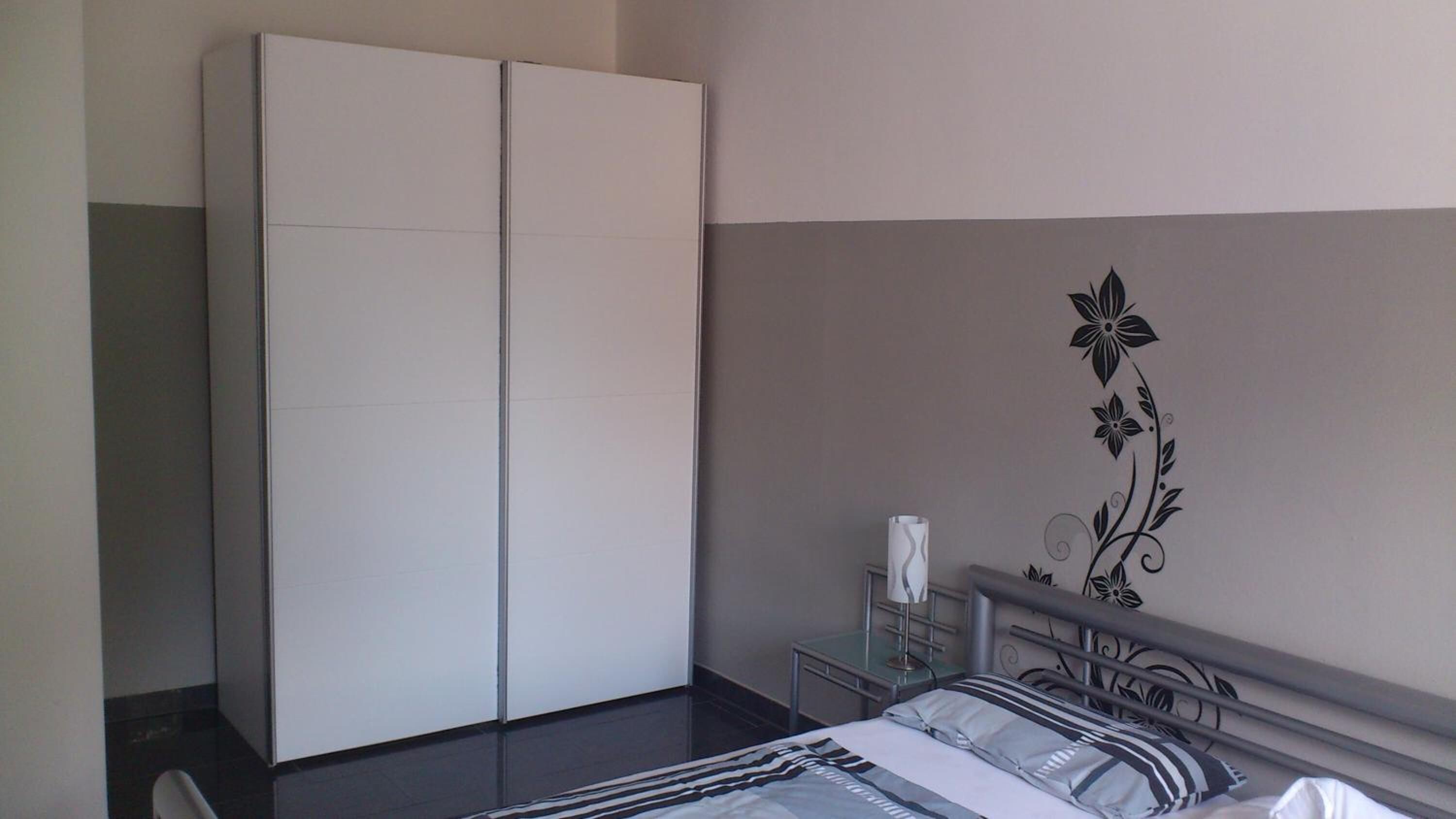 Un dormitorio con cama, armario, mesita de noche y un elemento decorativo en la pared.