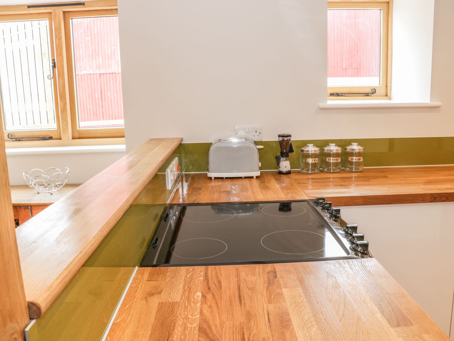 A kitchen with a black stove, wooden countertops, a toaster, and jars labeled tea, coffee, and sugar.