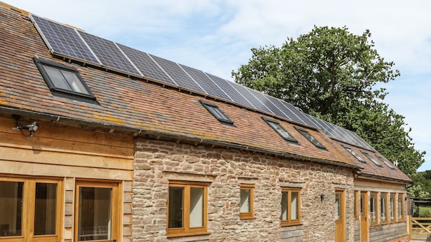 Un bâtiment en pierre doté d’un toit en pente, de panneaux solaires et d’une terrasse avec des meubles en bois.