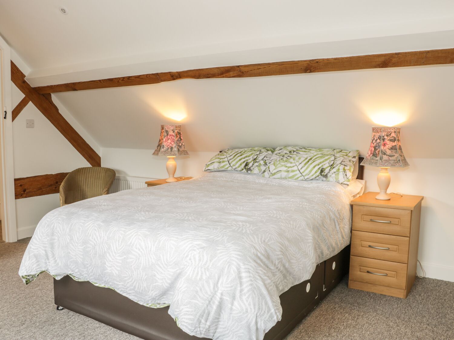 Ein Schlafzimmer mit einem großen Bett, zwei Nachttischlampen, einem Holznachttisch und einem Sessel.