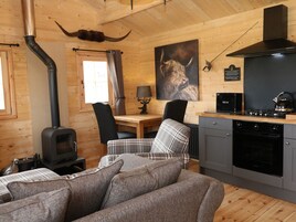 A cozy cabin interior with a fireplace, a dining area, a kitchen with modern appliances, and a large painting of a bull's head on the wall.