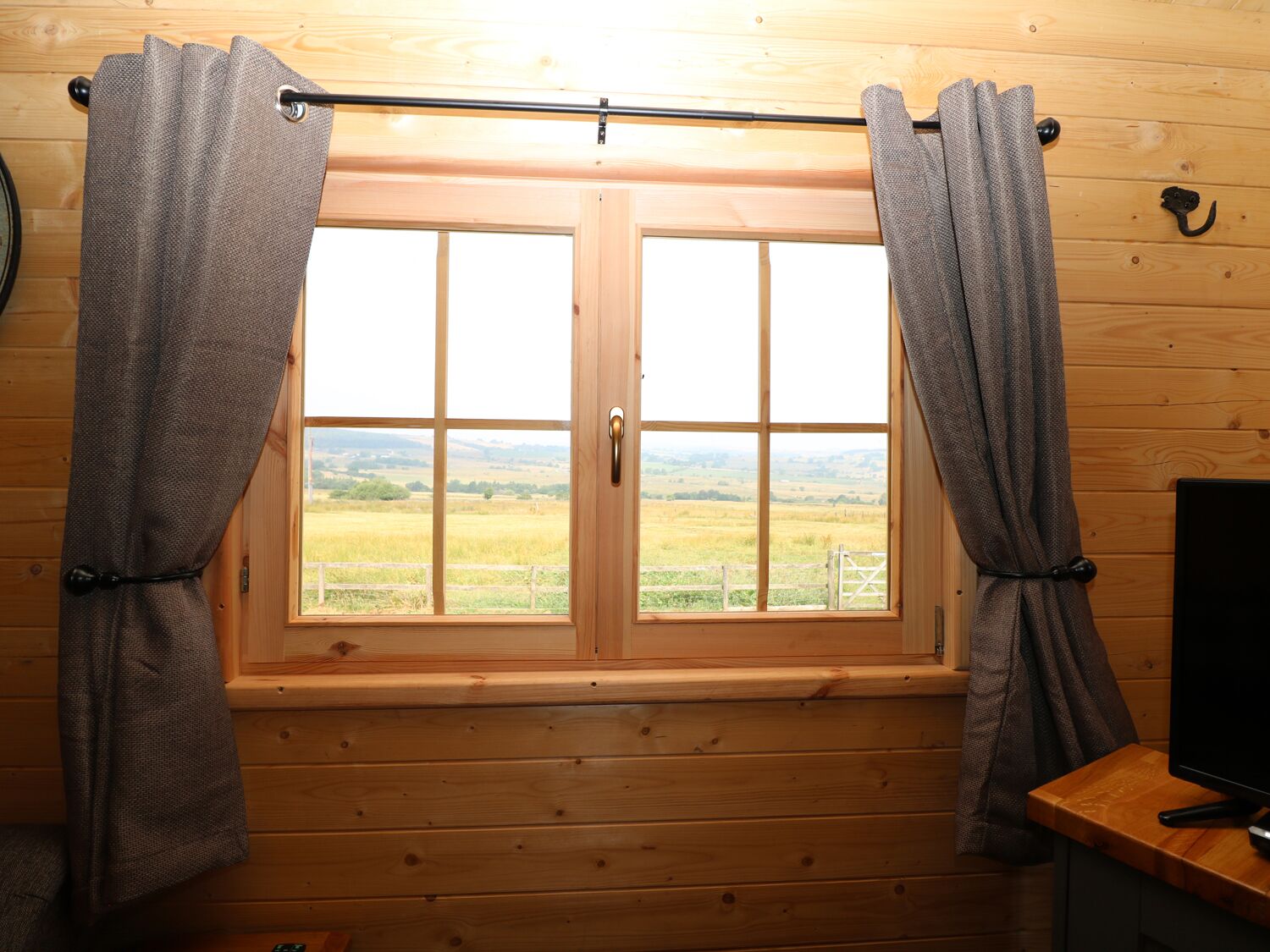 Ein Holzhütten-Zimmer mit großem Fenster, Vorhängen und einem Fernseher auf einem Holztisch.