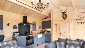 A cozy cabin interior with a kitchen, two plaid sofas, and a mounted deer head. - The Shooting Lodge (Buxton)