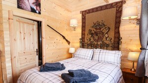 A wooden-paneled room with a bed, two bedside lamps, a tapestry, and a coat rack with a rifle. - The Shooting Lodge (Buxton)