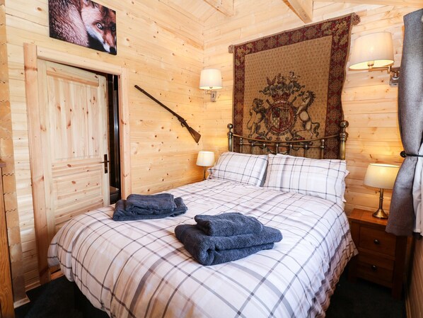 Habitación con paneles de madera, una cama, dos lámparas de noche, un tapiz y un perchero con un rifle.
