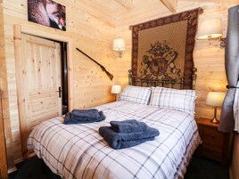Una stanza con rivestimenti in legno, un letto, due lampade da comodino, un arazzo e un appendiabiti con un fucile.