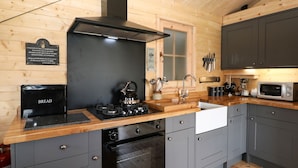 A modern kitchen with a wooden interior, a gas stove, an oven, a microwave, and grey cabinets. - The Shooting Lodge (Buxton)