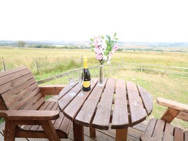 Un tavolo in legno con due sedie, una bottiglia di champagne e un vaso di fiori su un terrazzo affacciato su un prato.