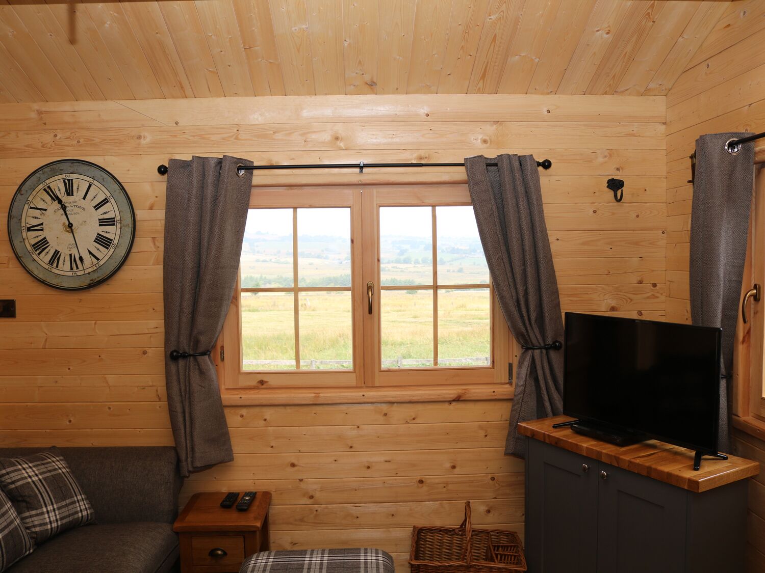 Ein Holzblockbau-Innenraum mit großem Fenster, einer Uhr, einem Fernseher und einem Sofa.