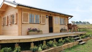 A wooden cabin with a porch, a chimney, and a small garden area with plants and flowers. - The Shooting Lodge (Buxton)