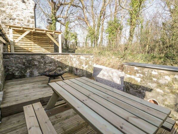 Une terrasse extérieure avec une table et des bancs en bois, des murs en pierre et un bâtiment en pierre en arrière-plan.