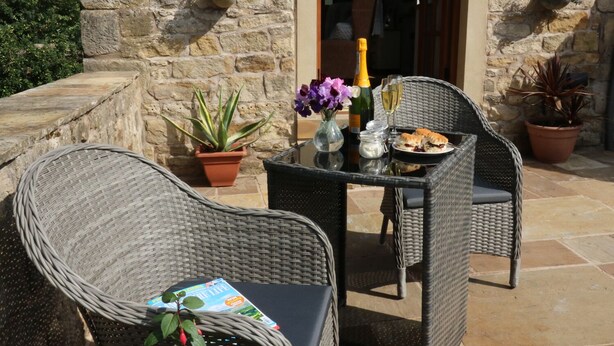 An outdoor seating area with wicker chairs and a table, a bottle of champagne, a glass of wine, and a plate of food. - Sunnybrook Cottage (Clitheroe)