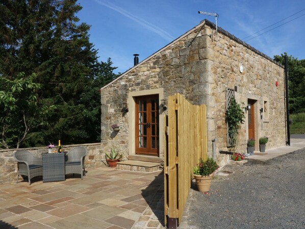 A stone building with a wooden door, a small porch with outdoor furniture, and potted plants.