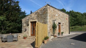 A stone building with a wooden door and a small porch area with outdoor furniture. - Sunnybrook Cottage (Clitheroe)