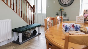 A dining area with a wooden table, chairs, and a bench. A large wall clock is visible. - Todlaw Farm House (Jedburgh)