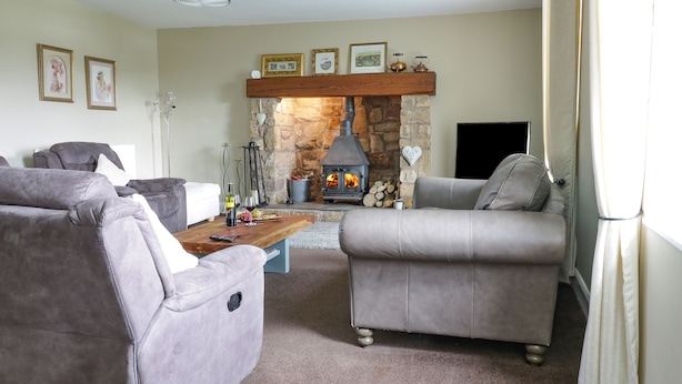 A cozy living room with a stone fireplace, two grey sofas, a wooden coffee table, and framed pictures on the wall. - Todlaw Farm House (Jedburgh)