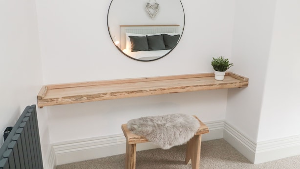 Un coin de pièce avec un banc en bois, un petit tabouret, un miroir et une étagère sur laquelle est posée une plante.