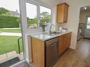 A kitchen with a dishwasher, sink, and wooden cabinets. - Bay View (Tyn-y-Gongl)