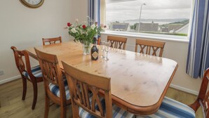 A dining room with a wooden table, six chairs, a vase with flowers, and a wall clock. - Bay View (Tyn-y-Gongl)
