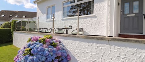 Un edificio blanco con una puerta gris, una ventana y una pequeña mesa con sillas.