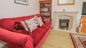 A living room with a red sofa, a fireplace, a bookshelf, and a mirror. - Bay View (Tyn-y-Gongl)