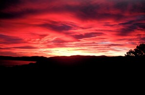 Ein Sonnenuntergang über einer Berglandschaft mit Baum-Silhouetten und einem Gewässer.