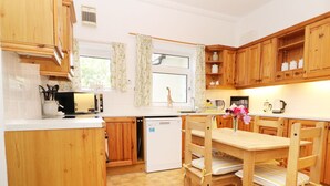 A compact kitchen with wooden cabinets, a white refrigerator, a dishwasher, and a dining table with chairs.