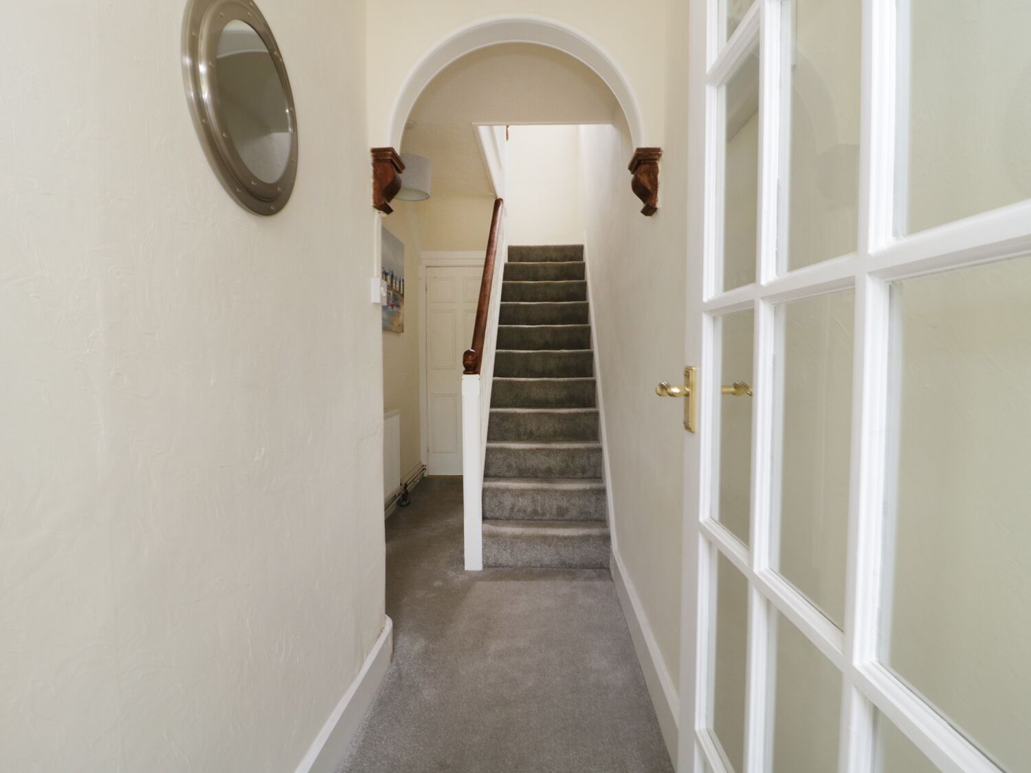 A hallway with a carpeted staircase leading to a door with glass panels.