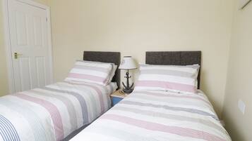 Une chambre avec deux lits, chacun doté de draps à rayures, une table de chevet avec une lampe et une porte.