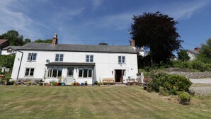 A two-story white building with a large front porch and a garden in front. - The Cottage (Llangollen)