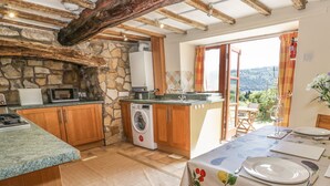 A kitchen with a stone wall, wooden cabinets, a washing machine, and a dining area with a table set for two. - The Cottage (Llangollen)