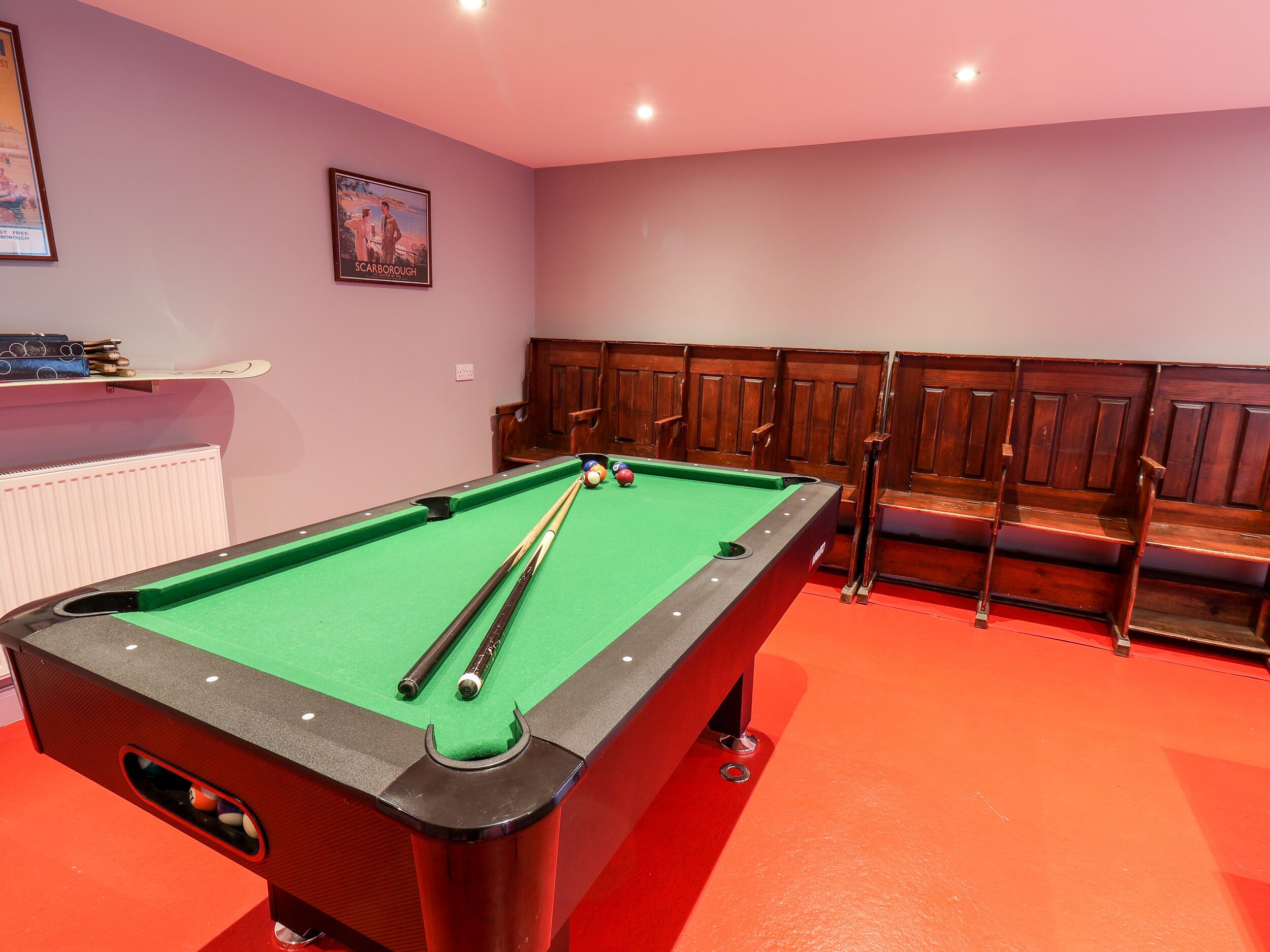 Une table de billard recouverte d’un drap vert, entourée de bancs en bois et posée sur un sol recouvert d’une moquette rouge.